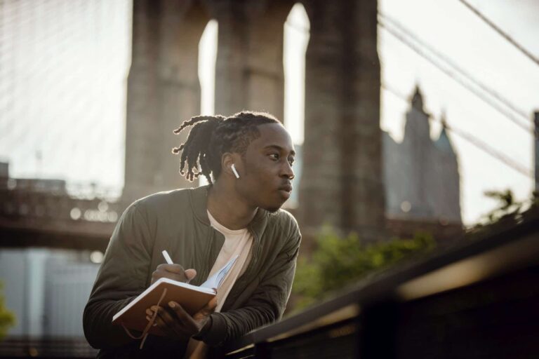 black man writing in a book sitting outside