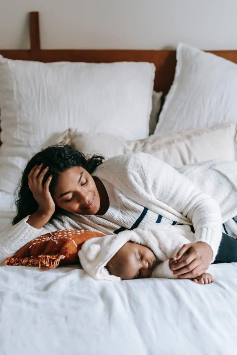 smiling young ethnic mother looking at sweet baby sleeping on bed