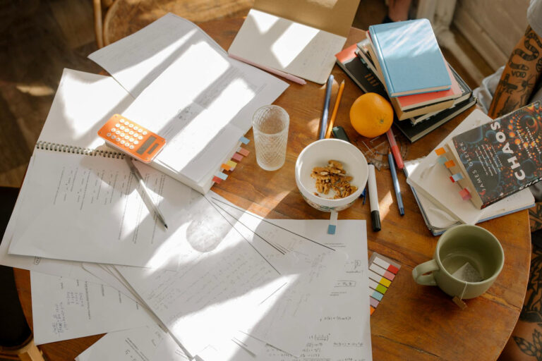 a light brown desk of notebooks, water, books almost like a busy person's desk