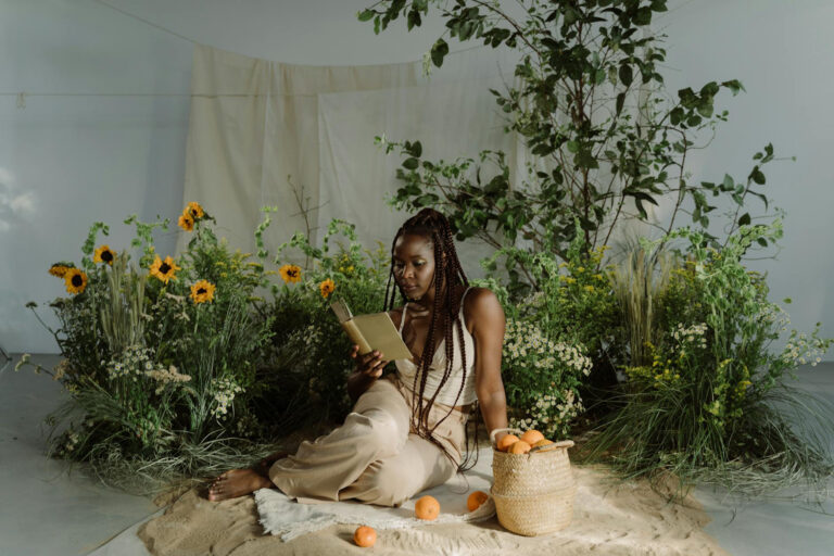 a beautiful black woman reading a book surrounding by lace curtains, plants, and sunflowers